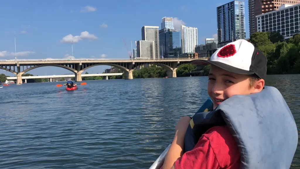 Child kayaking at Lady Bird Lake with the view of beautiful downtown Austin in the background