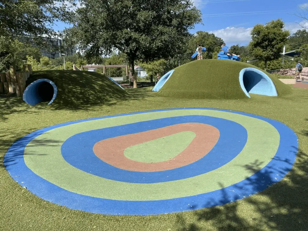 Kids playing on turf hills and tunnels at Alliance Children’s Garden in Austin, Texas