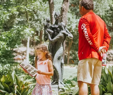 A child reads a book in front of a sculpture at Umlauf Family Day